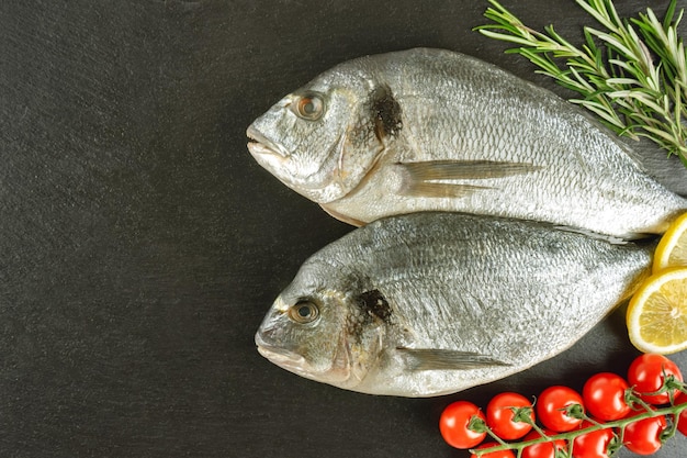 Pesce fresco dorado su sfondo nero ardesia con ingredienti per cucinare