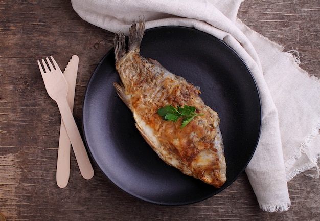 Pesce fritto (carpa) su un piatto nero decorato con prezzemolo