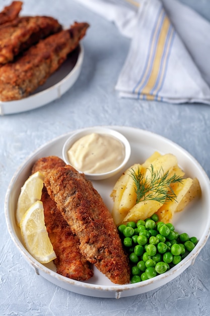 Pesce fritto con patate fritte piselli e limone