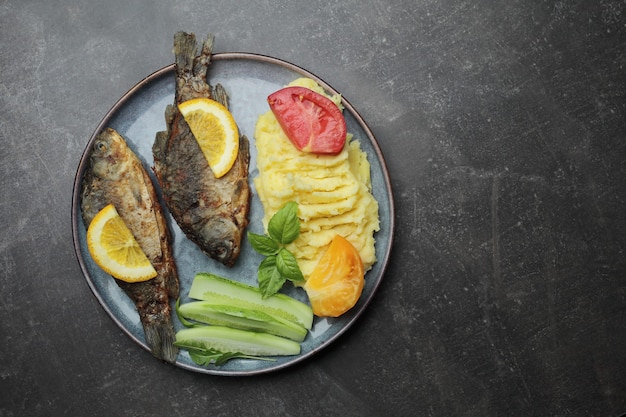 Pesce fritto e verdure su un piatto. Piano di lavoro grigio cemento.