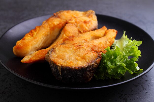 Pesce fritto su un piatto nero con lattuga