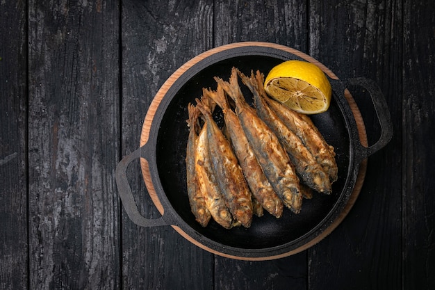 Pesce fritto su una padella di ghisa nera su un tavolo di legno scuro