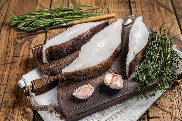 Pesce halibut atlantico, bistecche crude su tavola di legno con erbe aromatiche. Fondo in legno. Vista dall'alto.