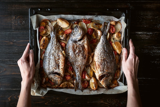 Pesce per cena in mani femminili pesce al forno su una teglia