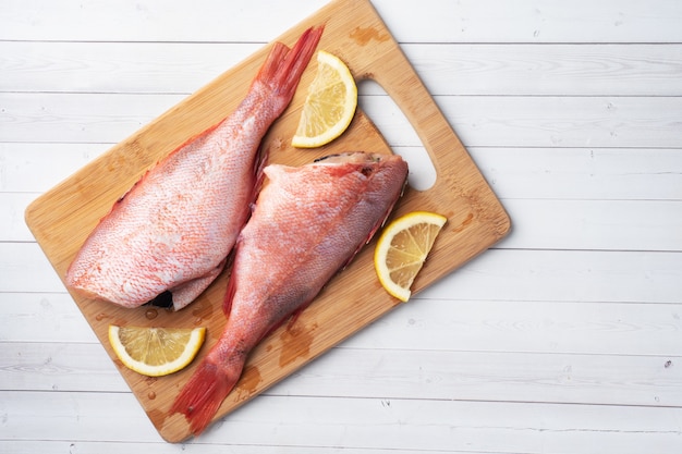 Pesce persico crudo senza testa con fette di limone e peperoncino rovente sul tagliere di legno