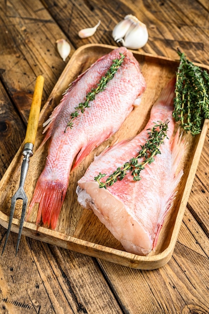 Pesce persico o branzino rosso intero crudo su un piatto. Tavolo di legno. Vista dall'alto.