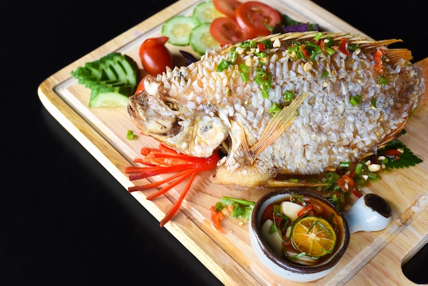 Pesce persico rosso grigliato in pastella con verdure e verdure su tagliere di legno isolato su dorso nero