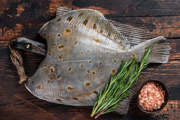 Pesce piatto crudo passera di mare sul bordo del macellaio con coltello. Fondo in legno scuro. Vista dall'alto.