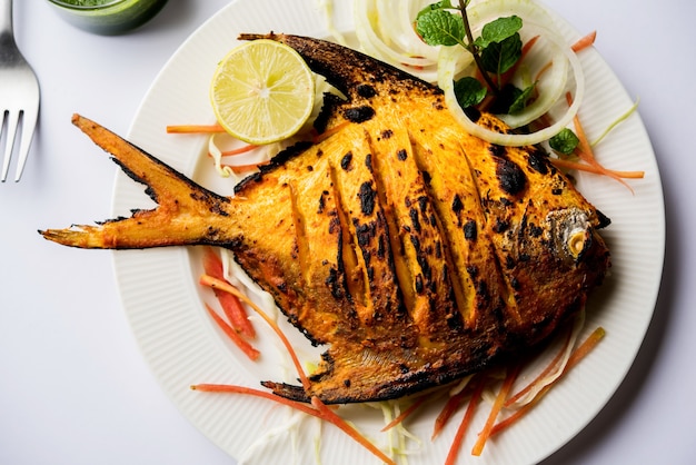 Pesce Pomfret Tandoori cotto in un forno di argilla e guarnito con insalata di limone, menta, cavolo e carote. Messa a fuoco selettiva