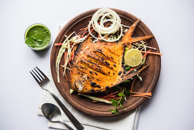 Pesce Pomfret Tandoori cotto in un forno di terracotta e guarnito con insalata di limone, menta, cavolo e carote