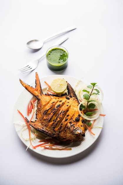 Pesce Pomfret Tandoori cotto in un forno di terracotta e guarnito con insalata di limone, menta, cavolo e carote