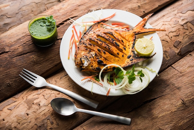 Pesce Pomfret Tandoori cotto in un forno di terracotta e guarnito con insalata di limone, menta, cavolo e carote