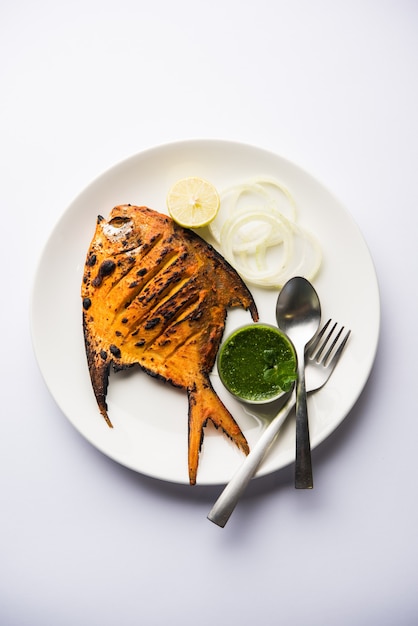 Pesce Pomfret Tandoori cotto in un forno di terracotta e guarnito con insalata di limone, menta, cavolo e carote