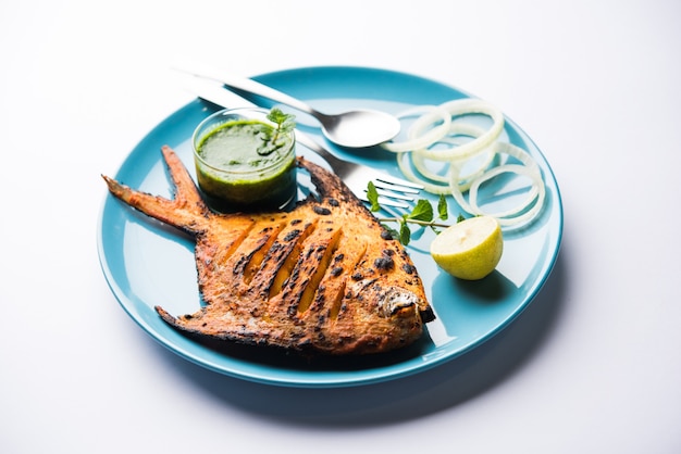 Pesce Pomfret Tandoori cotto in un forno di terracotta e guarnito con insalata di limone, menta, cavolo e carote