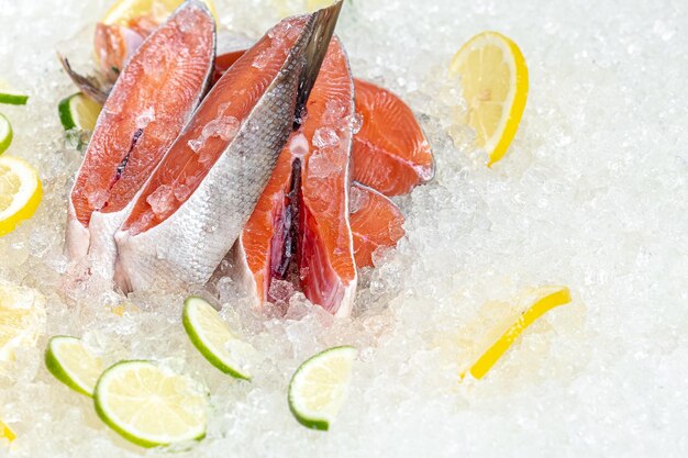 pesce rosso dell'oceano di mare fresco tagliato a pezzi, sdraiato sul ghiaccio, senza testa, ciliegia, limone a fette e lime