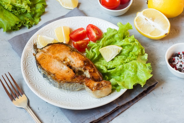 Pesce salmone al forno della bistecca su un piatto con gli ortaggi freschi.