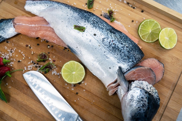 Pesce salmone crudo fresco sulla tavola di legno della cucina con spezie e lime