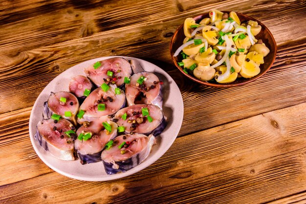 Pesce scomber affettato e funghi in scatola con cipolla verde su piatti di ceramica su tavola in legno rustico