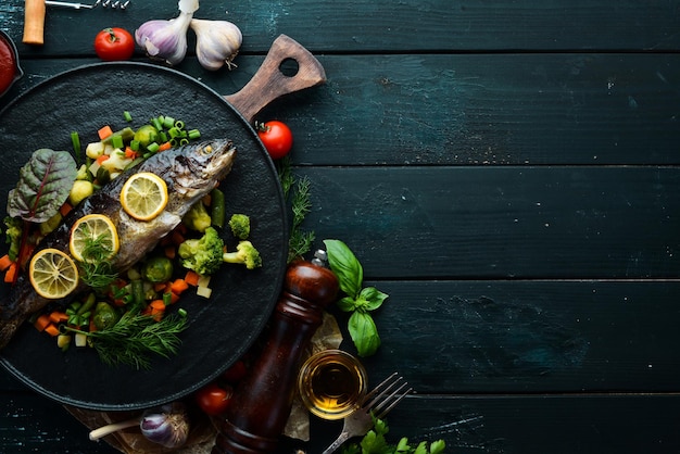 Pesce trota al forno con verdure e limone su un piatto nero Vista dall'alto Spazio libero per la copia