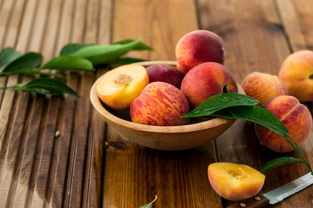 Pesche con foglie in una ciotola di legno con pesca a metà in cima Composizione piatta con pesche succose mature Raccolta di pesche per cibo o succo Vista dall'alto frutta fresca biologica cibo vegano