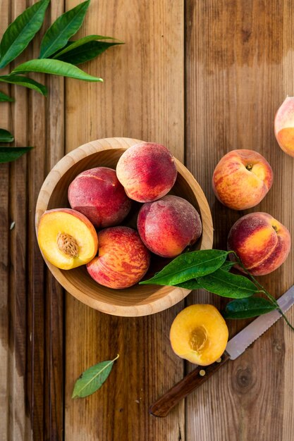 Pesche con foglie in una ciotola di legno con pesca a metà in cima Composizione piatta con pesche succose mature Raccolta di pesche per cibo o succo Vista dall'alto frutta fresca biologica cibo vegano