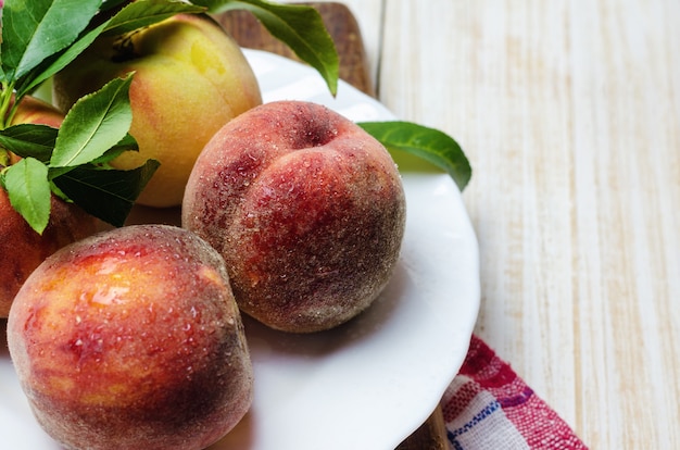 Pesche fresche in piatto bianco sulla tavola di legno