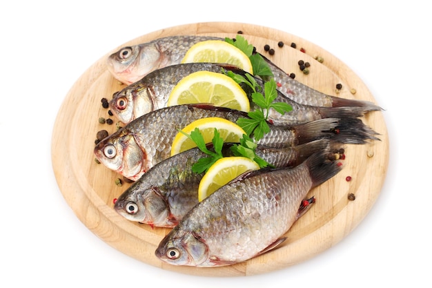 Pesci freschi con limone, prezzemolo e spezie sul tagliere di legno isolato su bianco