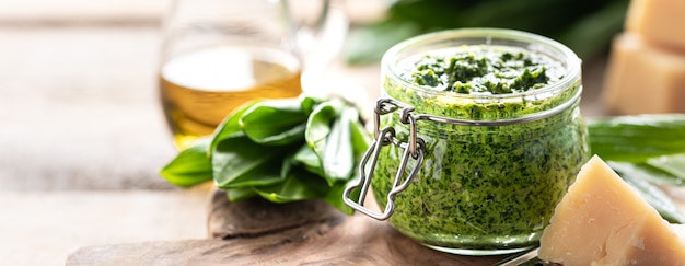 Pesto di porri selvatici con olio d'oliva e parmigiano in un barattolo di vetro su un tavolo di legno. Proprietà utili di aglio orsino. Foglie di aglio orsino fresco. Copia spazio