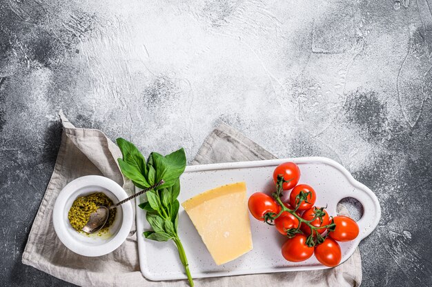 Pesto in mortaio di marmo, foglie di basilico e parmigiano su un tagliere.