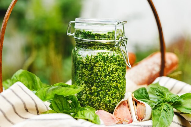 Pesto in un barattolo di vetro nel cestino da picnic all'aperto. Pesto tradizionale salsa italiana