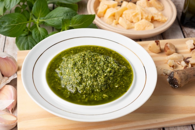 Pesto su un piatto bianco con parmigiano, aglio e basilico su una tavola di legno