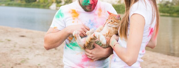 Pet, turismo estivo, festival holi e concetto di natura - primo piano di uomo e donna con gatto su sfondo naturale natural