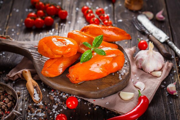 petti di pollo affumicati, spezie, verdure su un tagliere da cucina, scuro e lunatico, clouseup