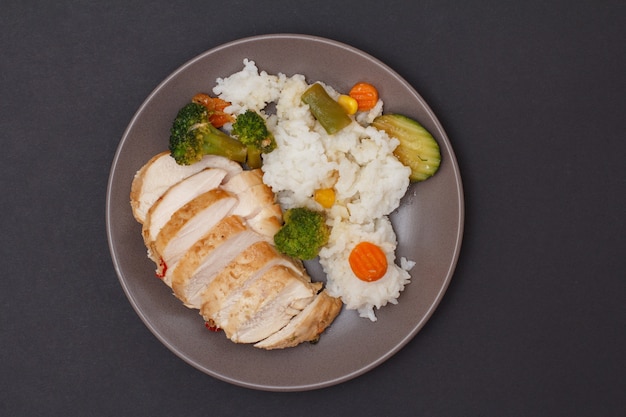 Petti di pollo al forno o filetto con riso, verdure e verdure su piastra e sfondo nero. Vista dall'alto.