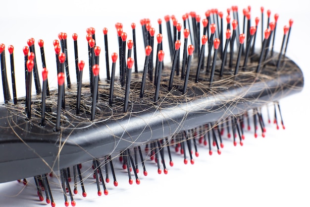 Pettine nero con capelli su sfondo bianco. Problema di caduta dei capelli. Avvicinamento.