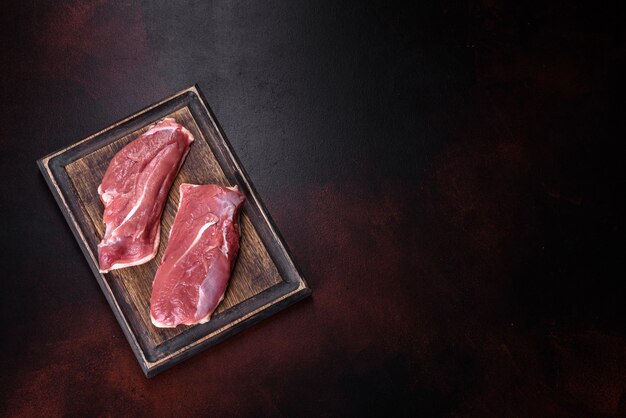 Petto d'anatra crudo con erbe e spezie su un tavolo scuro. Carne cruda preparata per la cottura