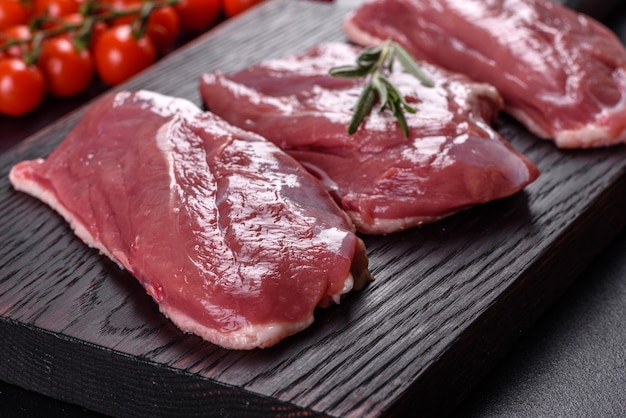 Petto d'anatra crudo con erbe e spezie su una superficie di cemento scuro. Carne cruda preparata per la cottura