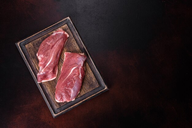 Petto d'anatra crudo con erbe e spezie su uno sfondo di cemento scuro. Carne cruda preparata per la cottura