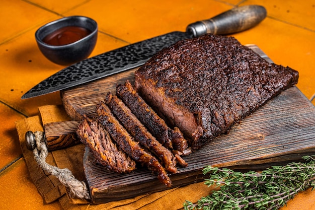 Petto di manzo barbecue affumicato con salsa su tavola di legno Sfondo arancione Vista dall'alto