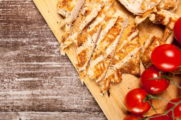 Petto di pollo affettato fresco alla griglia su tavola di legno accanto ai pomodori. Cena e stile di vita sani