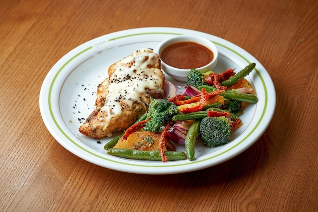 Petto di pollo al forno con formaggio e verdure bollite, broccoli in un piatto bianco su un tavolo di legno