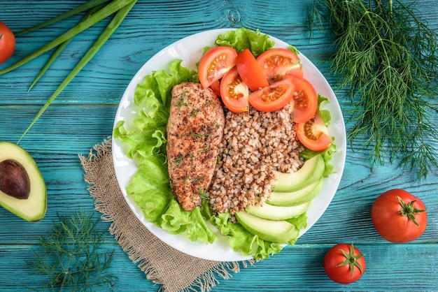 Petto di pollo alla griglia con porridge di grano saraceno, pomodori e avocado su legno blu