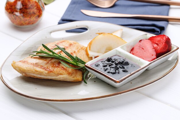 Petto di pollo alla griglia con salsa di frutti di bosco nel piatto sul tavolo in legno bianco clsoe up