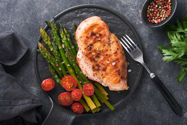 Petto di pollo alla griglia con verdure Bistecca di pollo alla griglia con asparagi e pomodorini in lamiera nera su sfondo grigio tavolo in cemento Pranzo dieta sana Bistecca barbecue fritta Vista dall'alto