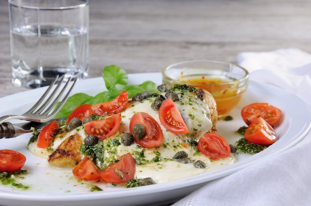 Petto di pollo alla griglia condito con mozzarella fusa, pesto di basilico, pomodoro e capperi