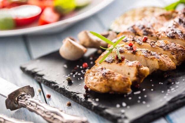 Petto di pollo alla griglia su tavola di ardesia, spinaci alle erbe, pomodori e altre verdure.