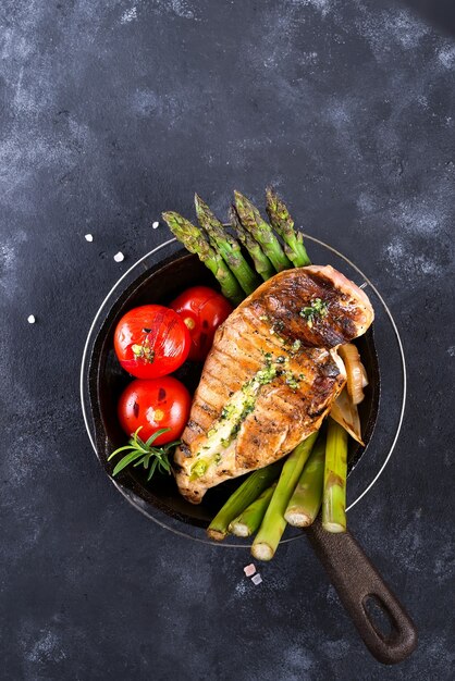 Petto di pollo alla griglia su una padella di ghisa con verdure grigliate su una superficie di pietra