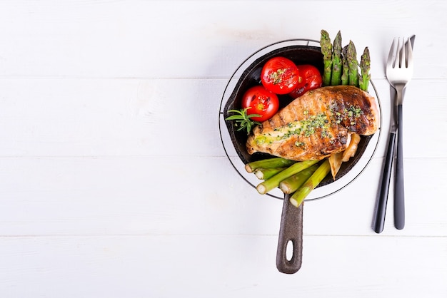 Petto di pollo alla griglia su una padella in ghisa con verdure grigliate su una superficie di legno