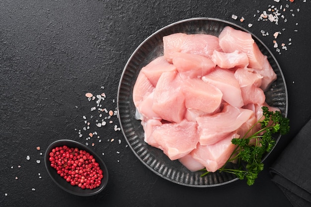 Petto di pollo crudo affettato o tagliato a pezzi su tagliere di legno con erbe e spezie su sfondo di cemento di pietra ardesia scura Carne di pollo cruda Vista dall'alto con spazio per la copia Mock up