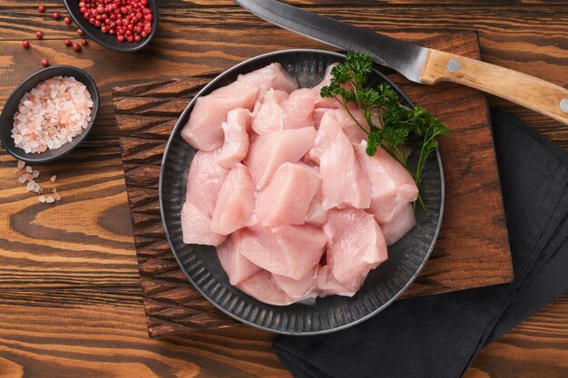 Petto di pollo crudo affettato o tagliato a pezzi su tagliere di legno con erbe e spezie su sfondo vecchio tavolo in legno Carne di pollo cruda Vista dall'alto con spazio di copia Mock up